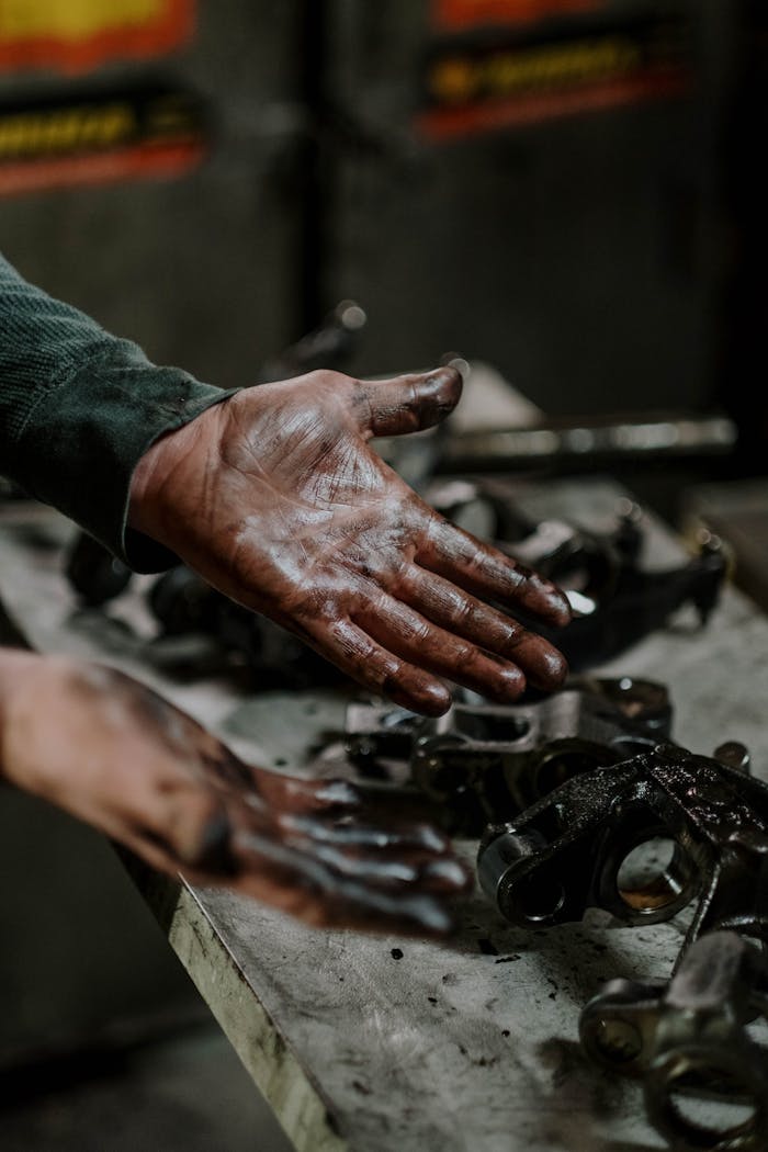 Close-up of a mechanic's hands covered in grease while working on engine parts in a workshop.